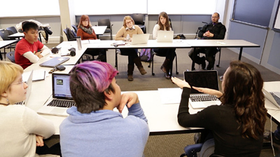 Several people in a classroom sitting at tables in a discussion.