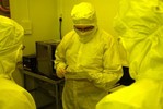 Man in clean suit inspects clean wafers.