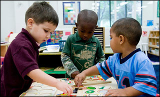 At a table, three small boys play with puzzles.