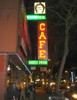 A cafe on an urban street at nighttime, people congregating on the street.