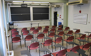 A view over several rows of tablet desks, showing the sliding chalkboards at the front of the classroom.