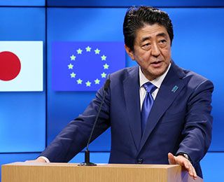 A middle-aged man, wearing a blue suit, stands at a podium.