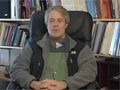 Professor Kip Hodges sitting in a chair with a wall of bookshelves behind him.