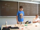 Student standing in front of blackboard with guitar physics equations behind him.