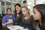 Girls sit around a laptop, one of them is using the mouse. A volunteer looks over her shoulder.