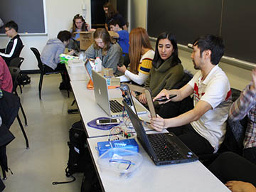 Students with their laptops sitting in a classroom discussing Arduino project ideas.